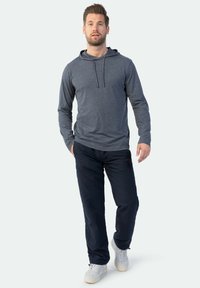 Graues Langarmshirt mit Kapuze, kombiniert mit marineblauen Hosen. Das Shirt hat eine Kapuze mit Kordelzug, während die Hosen seitliche Taschen und eine lockere Passform besitzen.