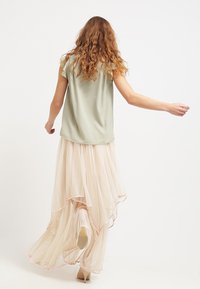 Lys grøn ærmeløs bluse sammen med en svajende, lagdelt, lys pink nederdel, der hviler lige over anklerne og har en bølget kant.