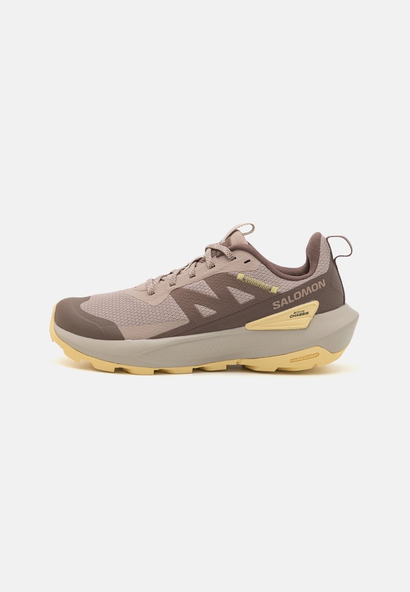 Brown and beige Salomon running shoe with lace-up design, mesh upper, thick beige sole, and branding on the side, shown from the outer side.