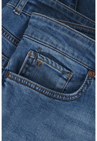 Modré džíny z denimu s prednou kapsou s žltým prešívaním a malým logom, ukazujúce textúrovanú tkaninu s bledým prevedením.
