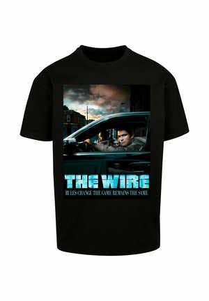 Sort bomulds t-shirt med grafik tryk af "The Wire". Billedet viser karakterer i en bil, med blå tekst der siger "REGLERNE ÆNDRER SIG, MEN SPILLET FORBLIVER DET SAMME."