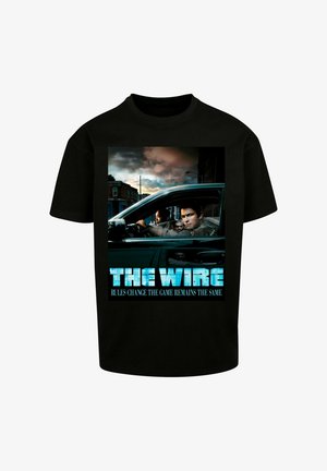 Sort bomulds t-shirt med grafik tryk af "The Wire". Billedet viser karakterer i en bil, med blå tekst der siger "REGLERNE ÆNDRER SIG, MEN SPILLET FORBLIVER DET SAMME."