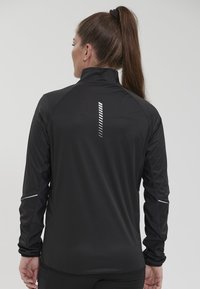 Svart atletisk jacka med hög krage, långa ärmar och reflektiva detaljer; har ett vertikalt randigt mönster på baksidan.