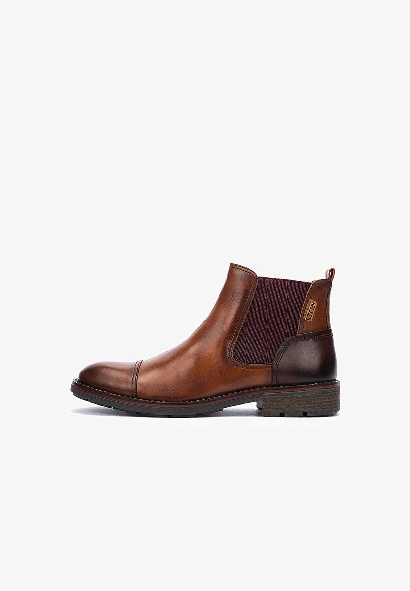 Bota Chelsea de cuero marrón con paneles laterales elásticos, punta redonda, tacón en un marrón oscuro contrastante y acentos texturizados en la parte superior.