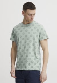 Lys grønn bomulls t-skjorte med korte ermer, med et mønster av mørke sirkulære design over hele og rund hals.