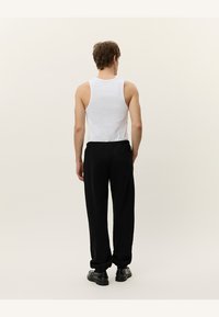 Camiseta sin mangas blanca combinada con pantalones de chándal negros, con un ajuste relajado y puños elásticos, vista desde la parte de atrás contra un fondo neutro.
