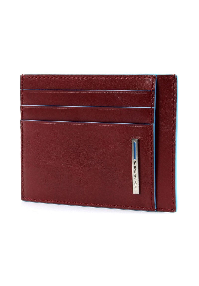 Billetera de cuero rojo con cuatro ranuras para tarjetas, costuras de acento azul y un logo plateado en el lateral. Diseño delgado y rectangular.