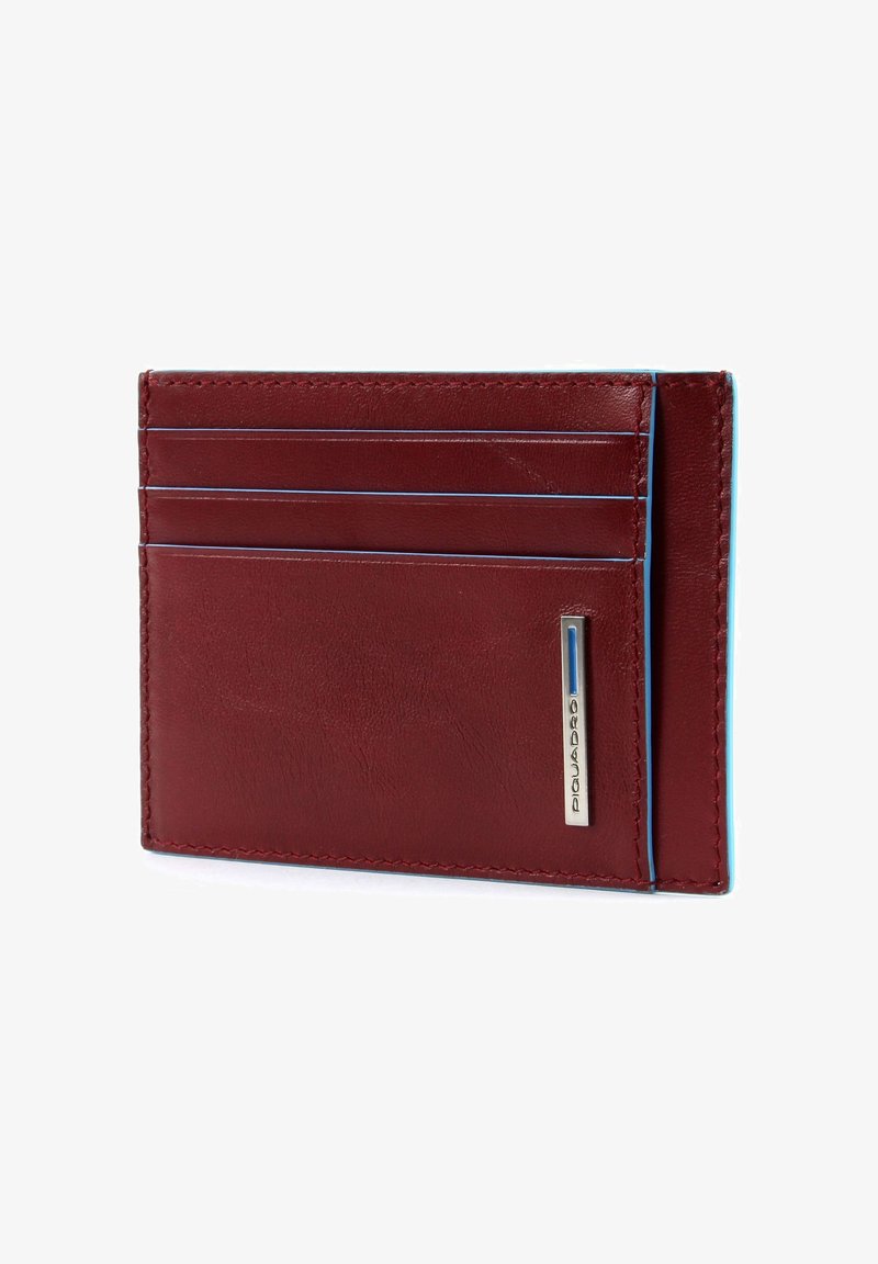 Portafoglio in pelle rossa con quattro slot per carte, cuciture blu a contrasto e un logo argentato sul lato. Design sottile e rettangolare.