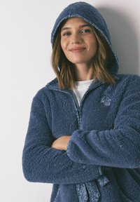 Navyblauwe, rits fleecejack met een capuchon, met een gestructureerd, luchtig oppervlak en een striksluiting in de taille. Sprankelende accenten zichtbaar.