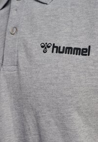 Szara koszulka polo z teksturowanej tkaniny, wyposażona w plisę na trzy guziki oraz wyszywane czarne logo "hummel" na lewej piersi.