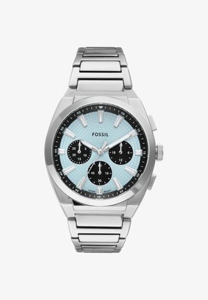 Montre-bracelet Fossil argentée avec cadran texturé bleu clair, trois sous-cadrans noirs, index lumineux et bracelet métallique à maillons.