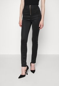 Black stretchy trousers with a fitted design, featuring a front zip closure and smooth texture. Paired with black pointed-toe heels.