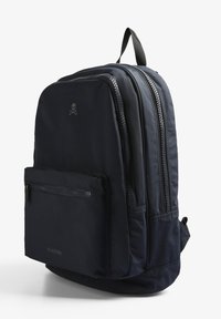 Mochila navy con cremalleras dobles, bolsillo delantero con cremallera, sutil logo de calavera y tela texturizada. Correas ajustables para mayor comodidad.