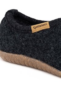 Sorte uldsko med en tekstureret overdel, en beige lædermærke med "Gottstein" og en brun gummisål med rillede detaljer.