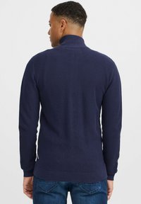 Námornícke modrý pletený sveter s vysokým golierom, textúrovaná látka, rebrované manžety a spodný lem, s bočnými švami s malými akcentmi.