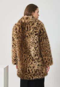 Leopardin kuvioinen tekoturkis takki, jossa on pehmeä pinta, löysä istuvuus ja leveä kaulus. Takissa on pitkät hihat ja helma, joka ulottuu lantiolle.