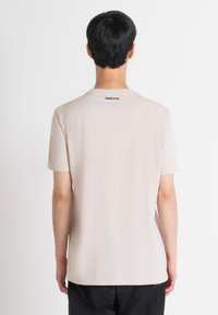 Camiseta corta de manga corta en beige claro con un cuello redondo, que presenta una etiqueta negra "MORATO" en la parte posterior. Está hecha de una tela suave.