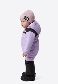 Dětská zimní kombinéza má lila horní část s černým panelem na ramenou, elastické manžety a černé zateplené nohavice. Doplněno růžovou pletenou čepicí.