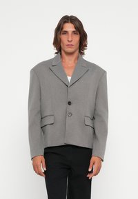 Gray cropped blazer with wide shoulders, notch lapel, two front pockets, and two-button closure; textured fabric finish.