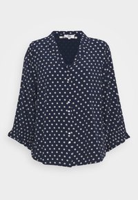 Marinblå skjorta med V-ringning, trekvartsärmar och vitt prickmönster. Lättviktsmaterial med knappar framtill.