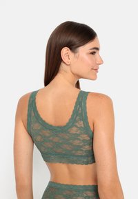 Brassière en dentelle verte avec une texture douce et translucide ; dotée de larges bretelles et de bords festonnés, mettant en valeur des motifs floraux sur l'ensemble.