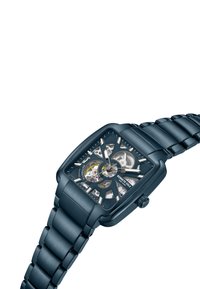 Kwadratowy niebieski metalowy zegarek z przezroczystą tarczą ukazującą wewnętrzne mechanizmy, srebrne akcenty oraz bransoletę w stylu ogniw.