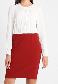 Witte blouse met lange mouwen en een ronde halslijn, met een keyhole-detail, gecombineerd met een aansluitende rode kokerrok, van gladde stof, zonder patronen.