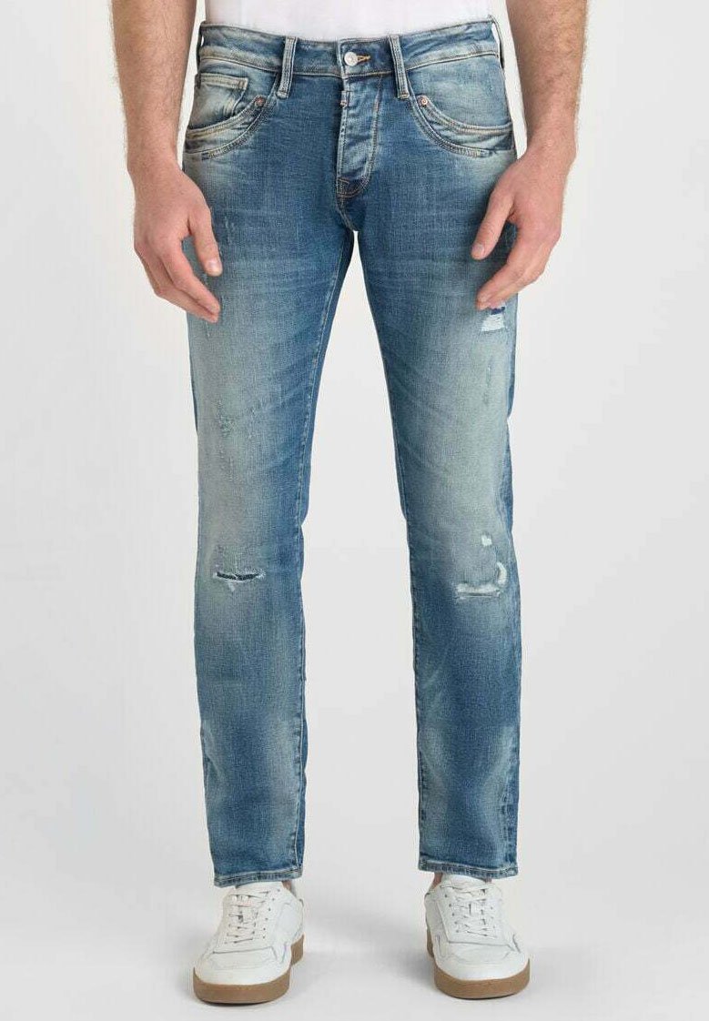 Jeans en denim bleu clair avec une coupe slim, présentant des détails déchirés et un effet décoloré. Le modèle porte des baskets blanches.