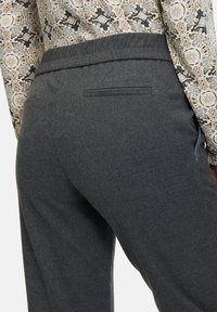 Graue, strukturierte Hose mit elastischem Bund und einer hinteren Tasche. Der Stoff wirkt weich und bequem.