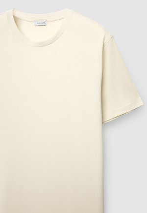 Maglietta color crema con scollo rotondo, maniche corte e superficie del tessuto strutturata. L'etichetta riporta la scritta "CALLIOPE."