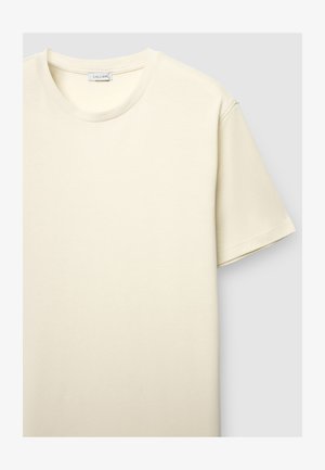 Maglietta color crema con scollo rotondo, maniche corte e superficie del tessuto strutturata. L'etichetta riporta la scritta "CALLIOPE."