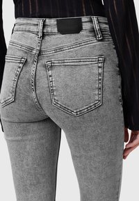 Harmaat farkkuhousut, joissa on korkea vyötärö, viisi taskua ja kontrastivärinen ompelu. Takavyötäröllä on merkitty musta nahkapläntti.