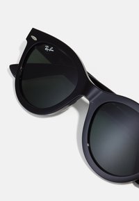 Melni pārliecinoši kaķu acs saulesbrilles ar tumšiem stikliem, izceļoties ar spīdīgu rāmi un izteiksmīgiem augšējiem stūriem. Uzlikts Ray-Ban logo.