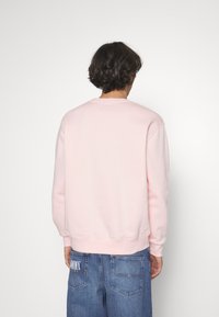 Sudadera rosa claro con cuello redondo, mangas largas y puños y dobladillo acanalados. Combinada con jeans de mezclilla azules que presentan un logo en la parte trasera.