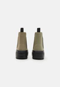 Green and beige ankle boots with a smooth rubber finish, black soles, and rear pull tabs for easy wear. Features side elastic panels.
