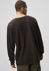 Koszula z długim rękawem w ciemnym brązie z poziomymi paskami, wykonana z miękkiej tkaniny, o luźnym kroju, z prążkowanymi mankietami i dekoltem.