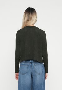Mørkegrønn ribbestrikket genser med lange ermer, cropped design, rund halslinning, kombinert med høyhalsede lyseblå jeans.