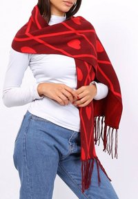Écharpe rouge en tissu doux, ornée d'un motif en forme de cœur et de lignes diagonales contrastantes. Les extrémités frangées ajoutent de la texture au design.
