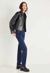 Fekete műbőr dzseki galléros kialakítással, sötétkék, egyenes szárú farmerrel és masszív fekete platform cipővel párosítva.