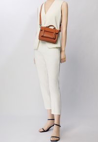 Torebka crossbody w kolorze brązowym ze skórki, z górną rączką i regulowanym paskiem, z klapką z przodu, zapięciem na zatrzask oraz subtelnymi detalami w postaci przeszyć.