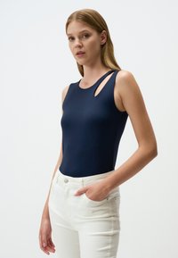 Body blu navy con scollatura tonda e dettagli a taglio su una spalla. Abbinato a jeans bianchi a vita alta. Tessuto morbido e liscio.