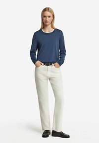 Granatowy sweter z długim rękawem, okrągłym dekoltem, w połączeniu z jasnymi, kremowymi spodniami o prostym kroju i czarnymi loafersami. Minimalistyczny design i dopasowanie.