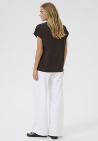 Brown short-sleeved top with a round neckline, worn with white wide-leg pants and black sandals, showcasing a relaxed fit and smooth texture.