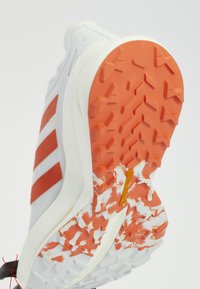 Semelle de chaussure de course avec une semelle à motif orange et blanc et trois bandes orange sur la tige blanche, montrant le logo Continental sur la semelle.