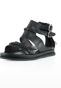 Sandale plate en cuir noir avec des brides à la cheville et aux orteils présentant des détails tressés et deux fermetures à boucle argentées sur le côté.
