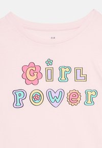 Ροζ πουκάμισο με πολύχρωμα, παιχνιδιάρικα γράμματα και λουλούδια που σχηματίζουν τη φράση «Girl Power» στο στήθος σε παστέλ τόνους.