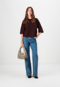 Bordeaux genser med boksercut, høytlivs blå jeans, og en beige toalettveske med slangeprint. Svarte sko. Enkelt, moderne silhuett med teksturkonstrast.