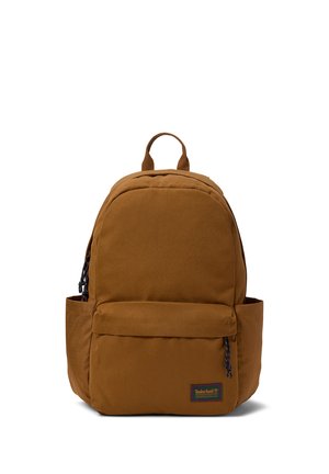Brun stofrygsæk med lynlåslomme foran, to sidelommer og et øverste håndtag, med en lille Timberland-logo-patch på frontlommen.