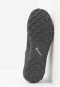 Schwarze Gummiaußensohle mit aggressivem Profil, ausgestattet mit verschiedenen schrägen Stollen für Halt, und einem Logo mit der Aufschrift "Michelin."