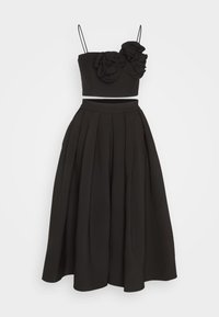 Ensemble noir deux pièces avec un top court orné d'appliques florales et de fines bretelles, associé à une jupe midi plissée taille haute.